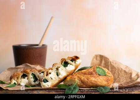 Hausgemachte, frisch gebackene, ruddige Spinatkuchen auf Backpapier, dekoriert mit frischen Spinatblättern, und eine Tasse Kaffee auf hellem Hintergrund Stockfoto