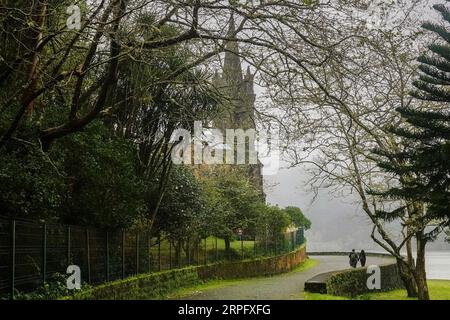 Ein Paar spaziert vorbei an der privaten Kapelle der Capela de Nossa Senhora das Vitórias am Furnas-See auf der Azoren-Insel Sao Miguel in Furnãs, Portugal. Stockfoto