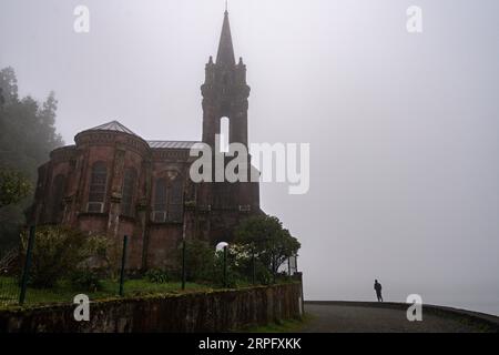 Ein Jogger, der vom Nebel umhüllt wird, geht an der gotischen Kapelle Our Lady of Victories am Furnas-See auf der Azoreninsel Sao Miguel, 30. März 2023 in Furnãs, Portugal, vorbei. Stockfoto