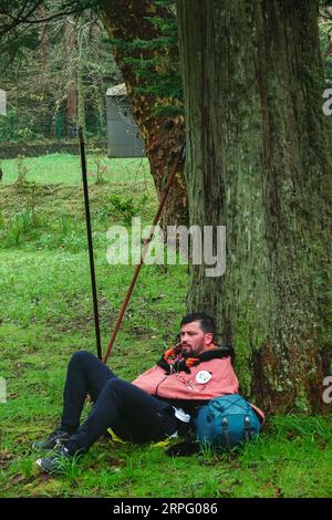 Ein erschöpfter römisch-katholischer Pilger, genannt Romeiro, ruht auf einem Baum während seiner 8-tägigen Wanderung um die Azoreninsel Sao Miguel, am 30. März 2023 in Furnãs, Portugal. Die Pilger besuchen 100 Schreine und Kirchen während der Veranstaltung aus dem Jahr 1522, als ein Erdbeben die ersten Siedlungen zerstörte. Stockfoto