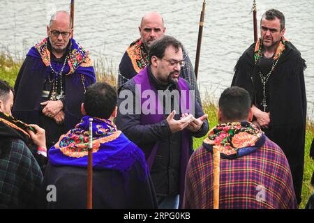 Ein römisch-katholischer Priester hält eine Predigt an Pilger, genannt Romeiros, am Ufer des Furnasees während ihrer 8-tägigen Wanderung um die Azoreninsel Sao Miguel, am 30. März 2023 in Lagoa das Furnãs, Portugal. Die Pilger besuchen 100 Schreine und Kirchen während der Veranstaltung aus dem Jahr 1522, als ein Erdbeben die ersten Siedlungen zerstörte. Stockfoto