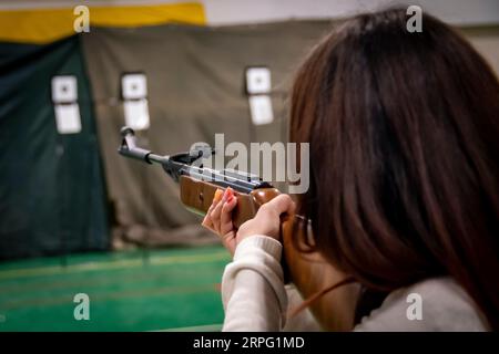 Braunhaariges Mädchen, das mit einem Luftgewehr auf ein Ziel schießt Stockfoto