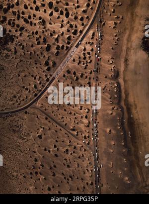 Luftaufnahme der Straße mit geparkten Autos an der Seite in trockenen Sanddünen. Draufsicht - vertikales Foto des Sandstrandes an der Küste mit Fahrzeugen auf der Straße. Stockfoto