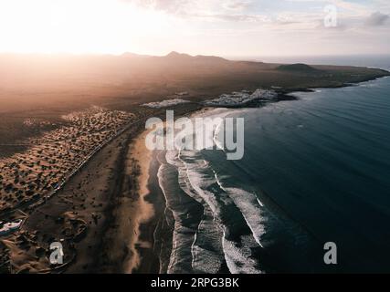 Luftaufnahme des Sonnenuntergangs auf Caleta de Famara auf den Kanarischen Inseln - Lanzarote: Breites Foto von oben mit starken Wellen im blauen Ozean und Sonnenuntergang am Himmel. Cl Stockfoto