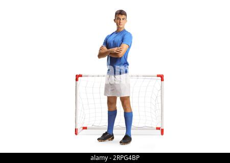 Portrait eines jungen Fußballspielers in einem blauen Trikot, der mit gefalteten Armen vor einem Minitor auf weißem Hintergrund posiert Stockfoto