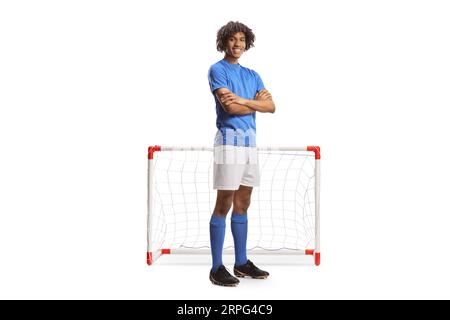 Portrait eines afroamerikanischen Fußballspielers in einem blauen Trikot, der mit gefalteten Armen vor einem auf weißem Backgro isolierten Minitor posiert Stockfoto