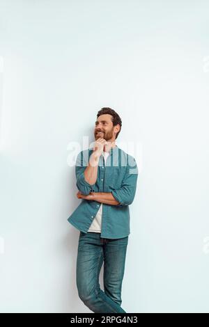 Der lächelnde Mann hält seine Hand an seinem Kinn und sieht auf weißem Hintergrund nachdenklich beiseite Stockfoto