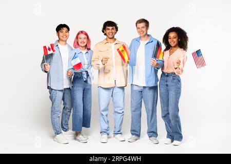 Glückliche Austauschschüler in der Sprachschule. Lächelnde, multirassische Freunde, die verschiedene Flaggen auf weißem Hintergrund halten Stockfoto