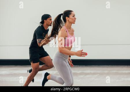 Zwei Athleten laufen zusammen im Freien. Frau und Mann sprinten auf dem Dach. Stockfoto