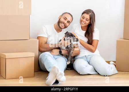 Wunderschönes junges, multirassisches Paar, das mit Hund spielt, Umzugstag Stockfoto