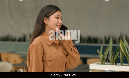 Seitenansicht Asiatische Geschäftsfrau lächelnd chinesische koreanisch japanische Frau Angestellte Manager gehen im Business Center sprechen Handy verhandeln Stockfoto