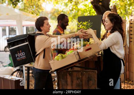 Bauernmärkte und Hauslieferungen. Einheimischer Landwirt schenkt Kurierinnen eine Box mit frischem Obst und Gemüse aus ökologischem Anbau und liefert gesunde, natürlich angebaute Lebensmittel an die Kunden Stockfoto