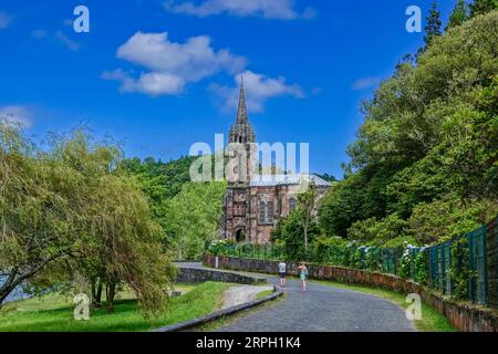 Ein Paar spaziert vorbei an der privaten Kapelle der Capela de Nossa Senhora das Vitórias am Furnas-See auf der Azoren-Insel Sao Miguel in Furnãs, Portugal. Stockfoto