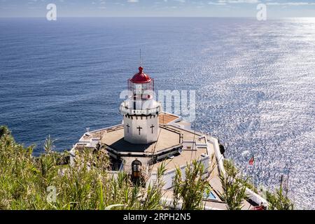 Blick auf den historischen Leuchtturm Farol Ponta do Arnel, der sich an den Klippen in Nordeste, Sao Miguel Island, Azoren, Portugal anschmiegt. Der noch aktive Leuchtturm war der erste, der 1876 auf den Azoren gebaut wurde. Stockfoto