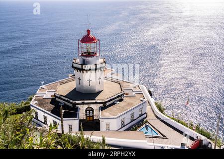 Blick auf den historischen Leuchtturm Farol Ponta do Arnel, der sich an den Klippen in Nordeste, Sao Miguel Island, Azoren, Portugal anschmiegt. Der noch aktive Leuchtturm war der erste, der 1876 auf den Azoren gebaut wurde. Stockfoto