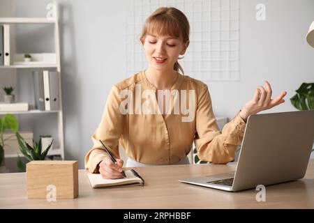 Junge Frau schreibt Notizen während Online-Vorstellungsgespräch zu Hause Stockfoto
