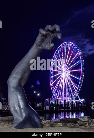 Die erwachende Skulptur in der Nacht mit dem im Hintergrund beleuchteten Hauptwalzrad, National Harbor, MD, USA Stockfoto