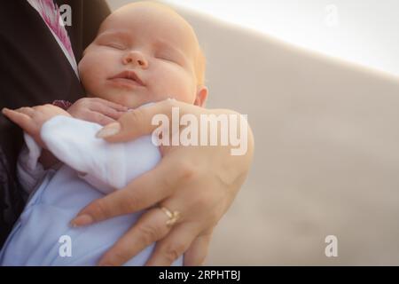 Mom wiegt ein Neugeborenes, das auf der Straße steht. Das Kind schläft in den Armen der Mutter Stockfoto