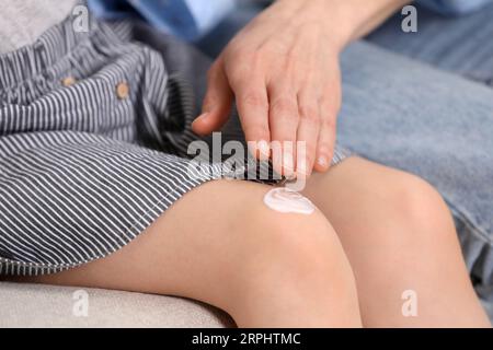 Mutter, die Salbe auf das Knie ihrer Tochter aufträgt, auf der Couch, Nahaufnahme Stockfoto