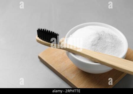 Bambuszahnbürste und Schüssel mit Backpulver auf grauem Tisch, Nahaufnahme. Platz für Text Stockfoto