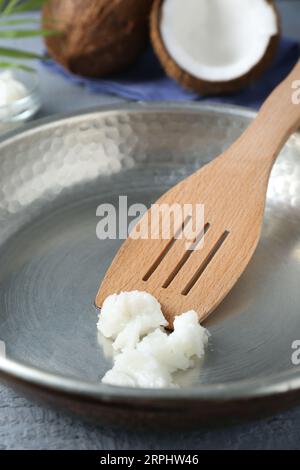 Bratpfanne mit Bio-Kokosöl und Holzspatel auf grauem Tisch, Nahaufnahme Stockfoto
