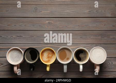 Viele verschiedene Tassen mit aromatischem Kaffee auf Holztisch, flach liegend. Leerzeichen für Text Stockfoto