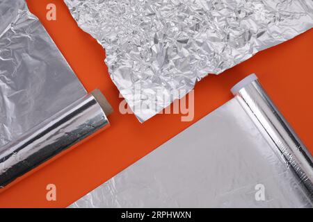 Verschiedene Rollen Aluminiumfolie auf orangem Hintergrund, flach liegend Stockfoto