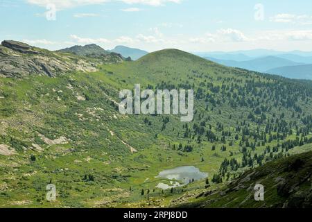 Ein kleiner See in einer Tiefebene, umgeben von hohen Bergen und Felsen an einem sonnigen Sommertag. Slonik Ridge und Mount Vidovka, Ergaki Nature Park, Krasnoyars Stockfoto