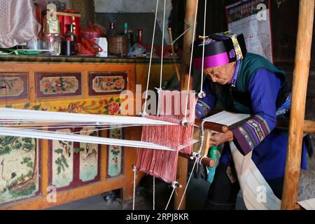 191201 -- SHILIN, 1. Dezember 2019 -- BI Xiuzhen, 75, webt Leinen im Dorf Danuohei der Gemeinde Guishan im autonomen Kreis Shilin Yi, südwestchinesische Provinz Yunnan, 28. November 2019. Danuohei Village, mit einer Geschichte von über 600 Jahren, ist ein gut geschütztes altes Dorf der Yi-ethnischen Kultur. Die Anwohner bauten Häuser und Straßen mit Steinen, was es als ein Steindorf einzigartig macht. Es ist umgeben von Bergen, Flüssen und einer wunderschönen Landschaft. Das Dorf hat heute 370 Haushalte mit einer Bevölkerung von 1.000, von denen 99,8 Prozent zur ethnischen Gruppe der Yi gehören. In den letzten Jahren haben die Einheimischen sich entschieden Stockfoto