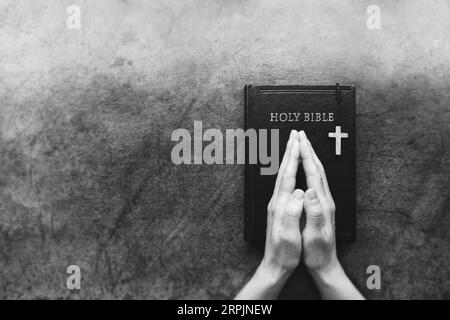 Christlicher Hintergrund mit dem Kreuz Jesu Christi auf dem Tisch und den Händen, die zusammen auf der heiligen Bibel stehen, meditieren, beten und verehren Stockfoto
