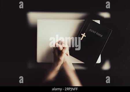 Christlicher Hintergrund mit Sonnenlicht, Fensterschatten, Hände zusammen in Meditation, Gebet und Anbetung neben dem Kreuz Jesu Christi und der Bibel. Stockfoto