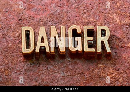 Gefahrenwort aus metallischen Buchstaben auf roter, rostiger Oberfläche Stockfoto