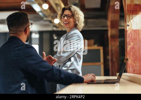 Technikprofis, die in einem Coworking-Büro miteinander sprechen. Zwei Geschäftsleute führen ein Gespräch an einem Arbeitsplatz. Stockfoto