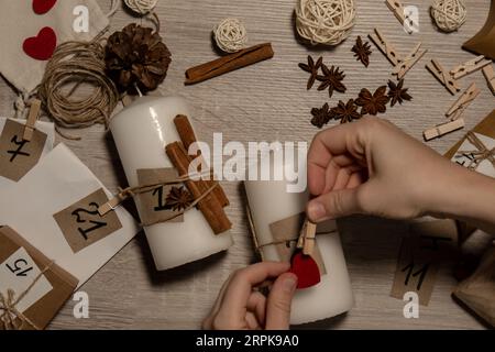 Eine nicht erkennbare junge Frau malt Zahlen auf Kerzen. Frau macht hausgemachte Adventskalender mit eigenen Händen gemacht Schritt für Schritt selbstgemachtes Kunsthandwerk Machen Sie es selbst. Vorbereitung auf das weihnachtskonzept. Saisonale Aktivitäten für Kinder, Familienurlaub im Winter. Umweltfreundlich Geschenke. Öffnen Sie das Paket jeden Tag Stockfoto