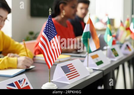 Nahaufnahme von Flaggen verschiedener Länder, die auf dem Tisch stehen, mit Studenten verschiedener Rassen, die im Hintergrund studieren Stockfoto