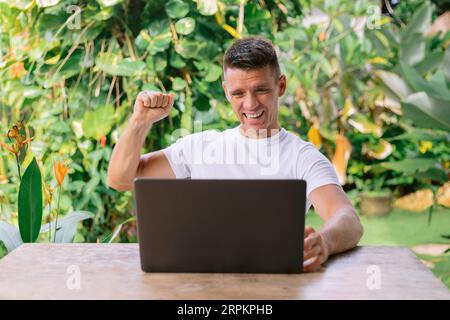 Fröhlicher Mann, der mit einem guten Angebot zufrieden ist. Glücklicher junger kaukasier fühlt sich euphorisch durch gute E-Mails, ein fantastisches Angebot oder Computerrabatt. Stockfoto