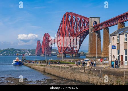 South Queensferry, Schottland, Großbritannien - 13. Mai 2023 - Personen auf dem Pier an der Forth Bridge über die Firth of Forth-Mündung, der berühmten freitragenden Eisenbahnbrücke von Stockfoto