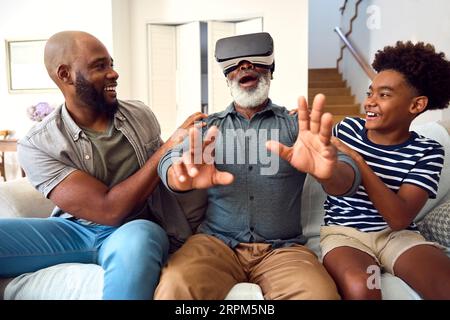 Großvater, der ein VR-Headset trägt, sitzt zusammen auf dem Sofa zu Hause Stockfoto