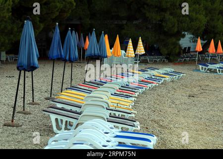 Bunte Sonnenschirme, die am Strand neben den Liegestühlen gefaltet wurden Stockfoto