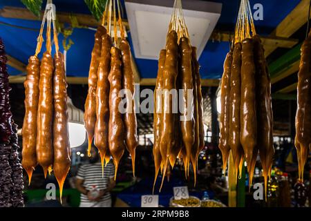 Eine Nahaufnahme von goldbrauner, getrockneter tschurtschchela (ჩურჩხელა) an einem Marktstand in Telavi, Kakheti. Die glatte, glänzende Schicht aus Pelamushi, die aus reduziertem Traubensaft ohne Zuckerzusatz hergestellt wird, verleiht der Süße ihre honigbraune Farbe; die deutlich sichtbaren Grate zeigen die einzelnen Schichten, die beim Tauchen entstehen. Ilia Chavchavadze Avenue, Gemeinde Telavi, Kakheti, 2200, Georgia Stockfoto