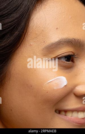 Nahaufnahme einer lächelnden asiatischen Frau mit dunklem Haar und Hautcreme auf ihrer Wange Stockfoto