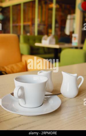 Frühstücksservice. Kaffee, Milch und Zucker in weißem Utensilien. Kaffeebecher und Milchkännchen auf dem Tisch im Café. Cafe-Innenausstattung. Weißes Geschirr. Stockfoto