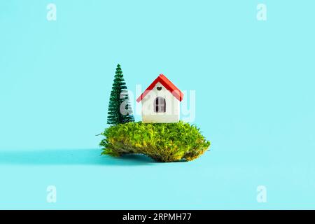Modell eines Hauses mit Grün auf blauem Hintergrund. Das Konzept des Wohnungsmarkts, Kauf oder Miete von Immobilien. Stockfoto