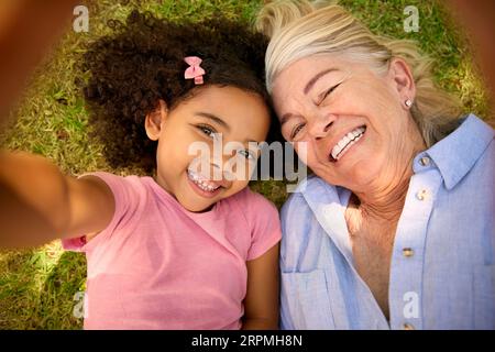 POV-Overhead-Aufnahme von Großmutter und Enkelin, die auf Grass liegen und Selfie auf dem Handy mitnehmen Stockfoto