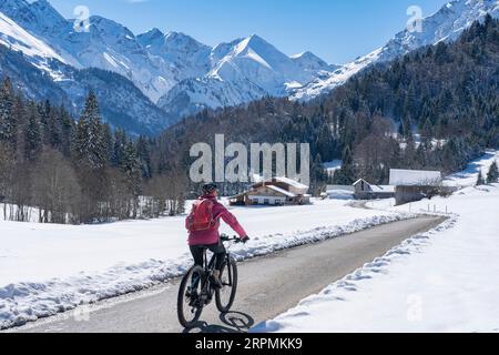 Nette Seniorin, die an einem sonnigen Wintertag in den Allgaeu-Alpen bei Oberstdorf, Bayern, mit dem E-Mountainbike unterwegs ist Stockfoto