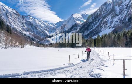 Nette Seniorin, die an einem sonnigen Wintertag in den Allgaeu-Alpen bei Oberstdorf, Bayern, mit dem E-Mountainbike unterwegs ist Stockfoto