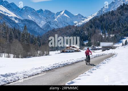 Nette Seniorin, die an einem sonnigen Wintertag in den Allgaeu-Alpen bei Oberstdorf, Bayern, mit dem E-Mountainbike unterwegs ist Stockfoto