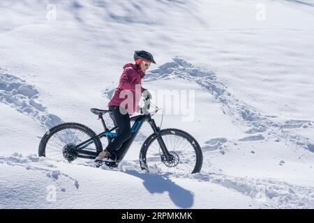 Nette Seniorin, die an einem sonnigen Wintertag in den Allgaeu-Alpen bei Oberstdorf, Bayern, mit dem E-Mountainbike unterwegs ist Stockfoto