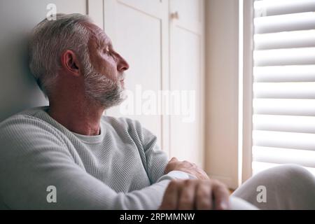 Nahaufnahme Des Depressiven Älteren Mannes, Der Mit Schlechter Psychischer Gesundheit Leidet, Der Zu Hause Auf Dem Boden Sitzt Stockfoto