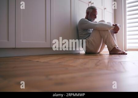 Depressiver Älterer Mann, Der Mit Schlechter Psychischer Gesundheit Leidet, Sitzt Zu Hause Auf Dem Boden Stockfoto